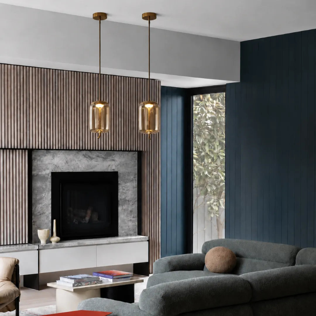 Dois pendentes âmbar Cognac em dupla sobre lareira em sala de estar com painel ripado e parede azul — Luminária Pendente Vidro Soprado LED Minimalista Bruma — Tonzi