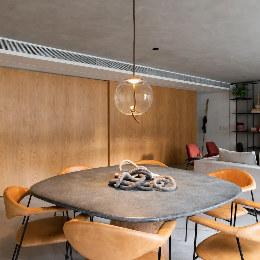 Pendente de vidro globo aceso sobre mesa de jantar de pedra com cadeiras de couro caramelo — Luminária Pendente Vidro Transparente LED Minimalista Clara — Tonzi