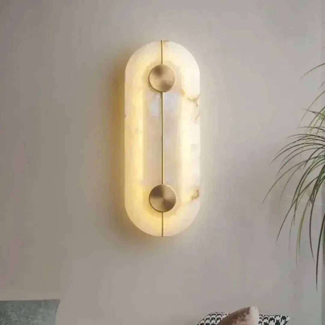 Arandela em mármore alabastro iluminada e instalada em parede cinza com planta ao fundo, ambiente residencial sofisticado — Arandela de parede mármore nórdica cobre luxo Alara — Tonzi