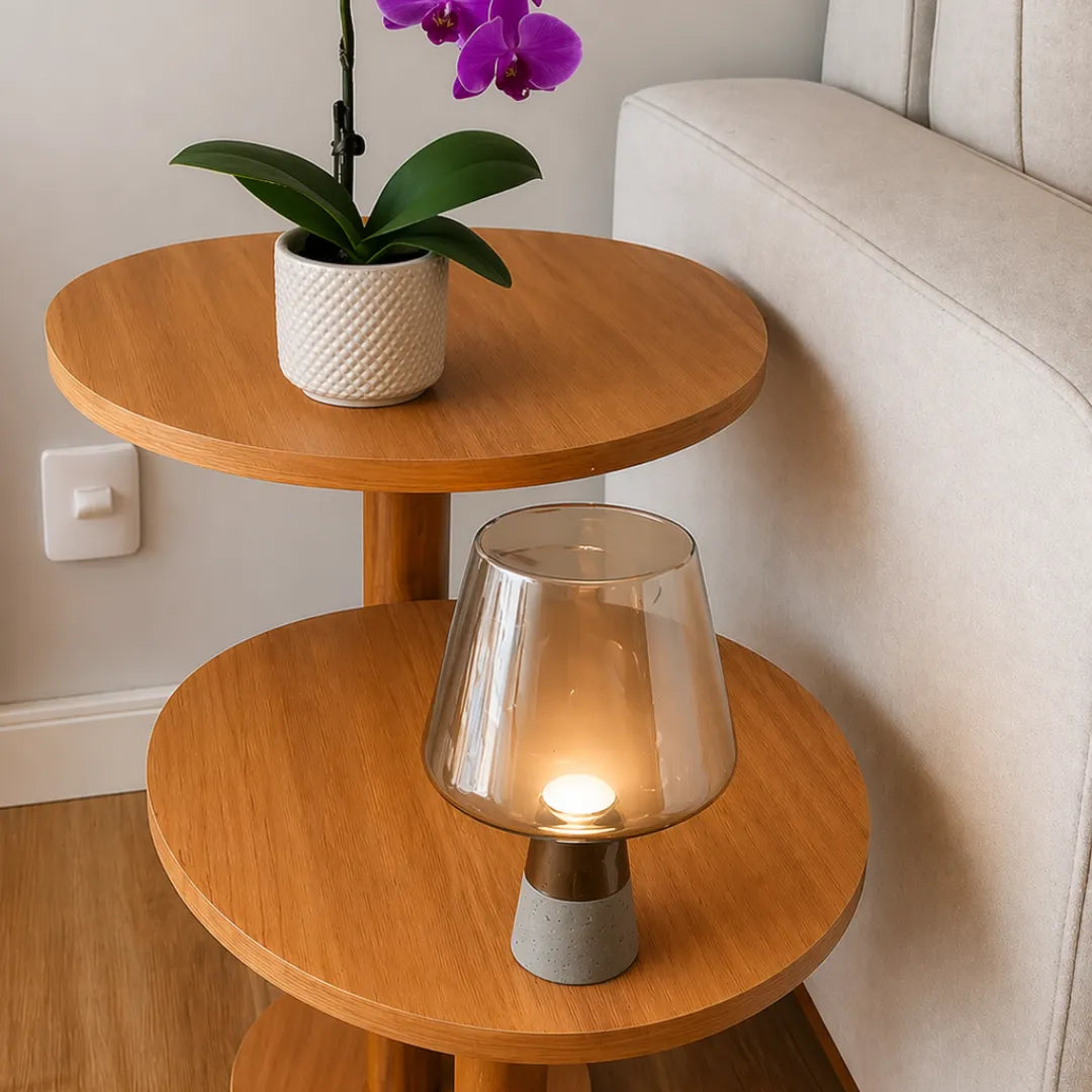 Luminária de mesa em vidro âmbar acesa em mesa lateral redonda de madeira clara ao lado de sofá bege e vaso com orquídea roxa em sala de estar — Luminária de Mesa Moderna Vidro Base Mármore — Tonzi