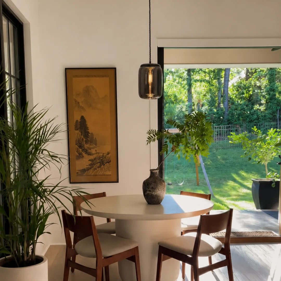 Pendente fumê aceso sobre mesa de jantar redonda clara em sala com vista para o jardim — Luminária Pendente Vidro Soprado LED Minimalista Bruma — Tonzi