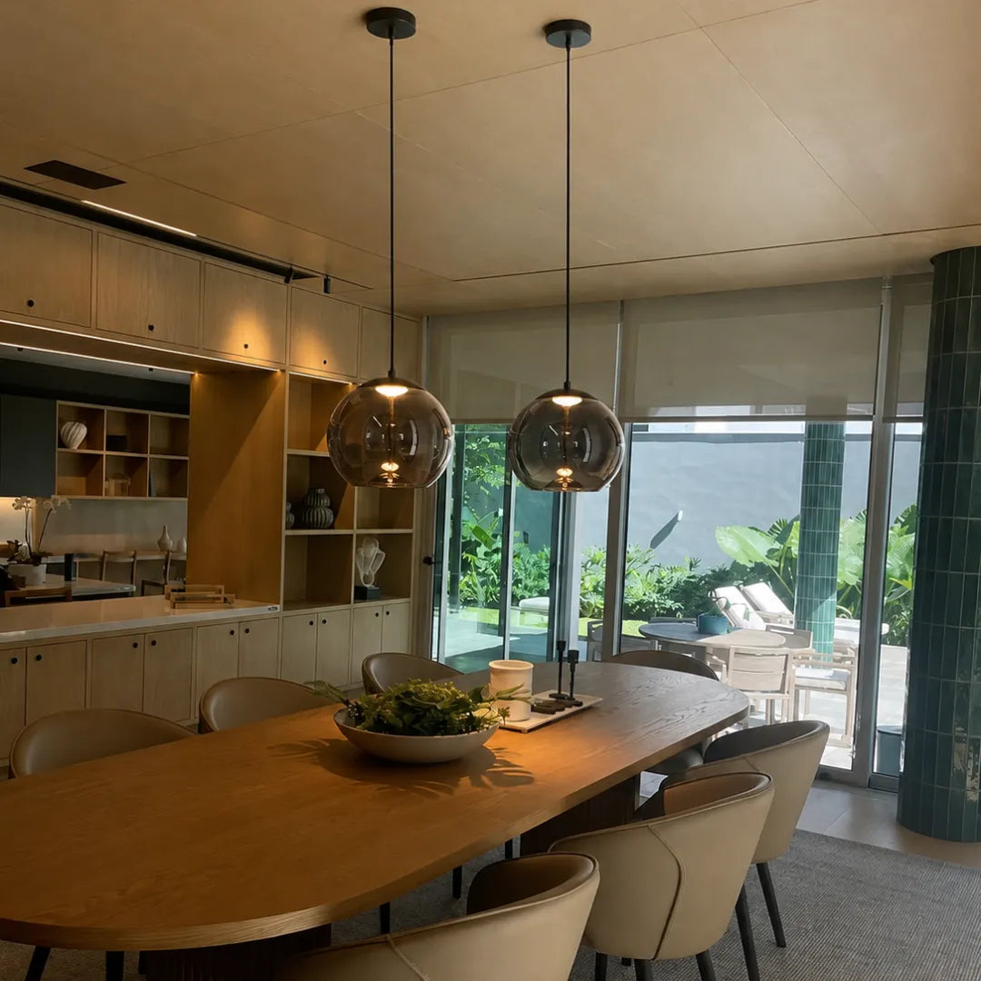 Dupla de pendentes esféricos âmbar Cognac sobre mesa de jantar de madeira com marcenaria clara e vista para o jardim — Luminária Pendente Vidro Soprado LED Moderna Brume — Tonzi