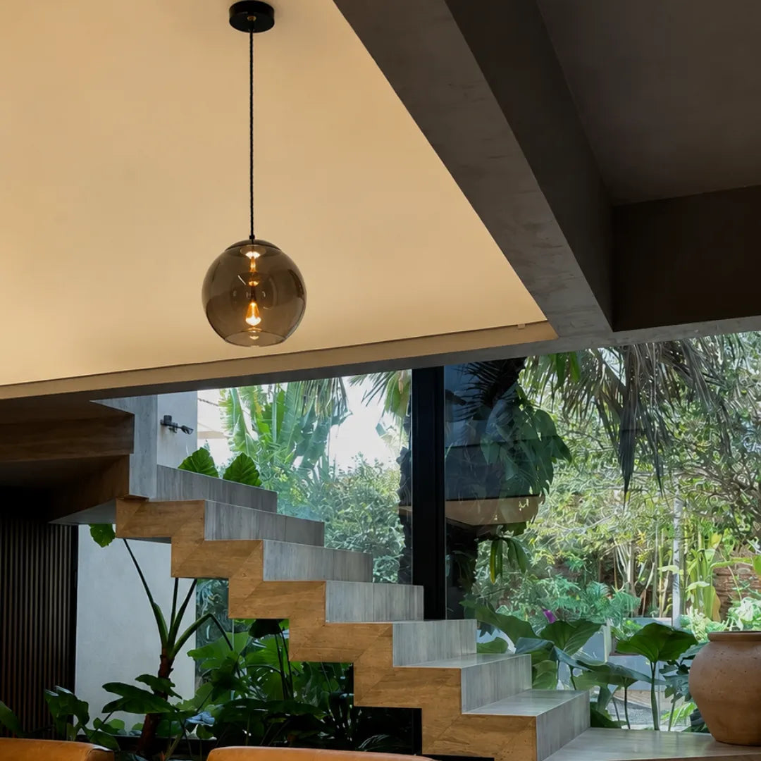 Pendente esférico fumê Smoke Gray sobre escada de concreto com jardim de inverno tropical — Luminária Pendente Vidro Soprado LED Moderna Brume — Tonzi