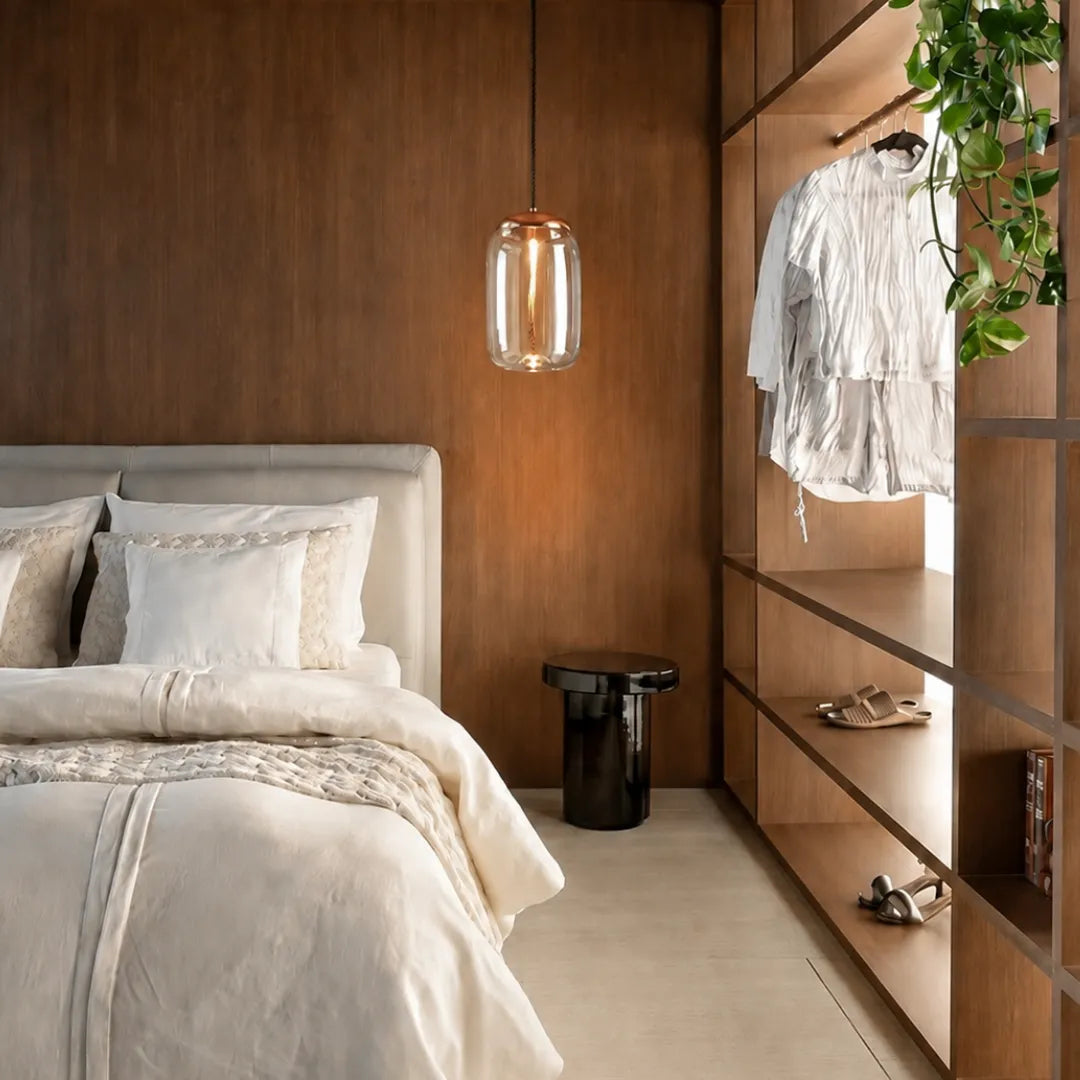 Pendente de vidro cilíndrico ao lado da cama em quarto com painel de madeira e closet aberto — Luminária Pendente Vidro Transparente LED Minimalista Clara — Tonzi