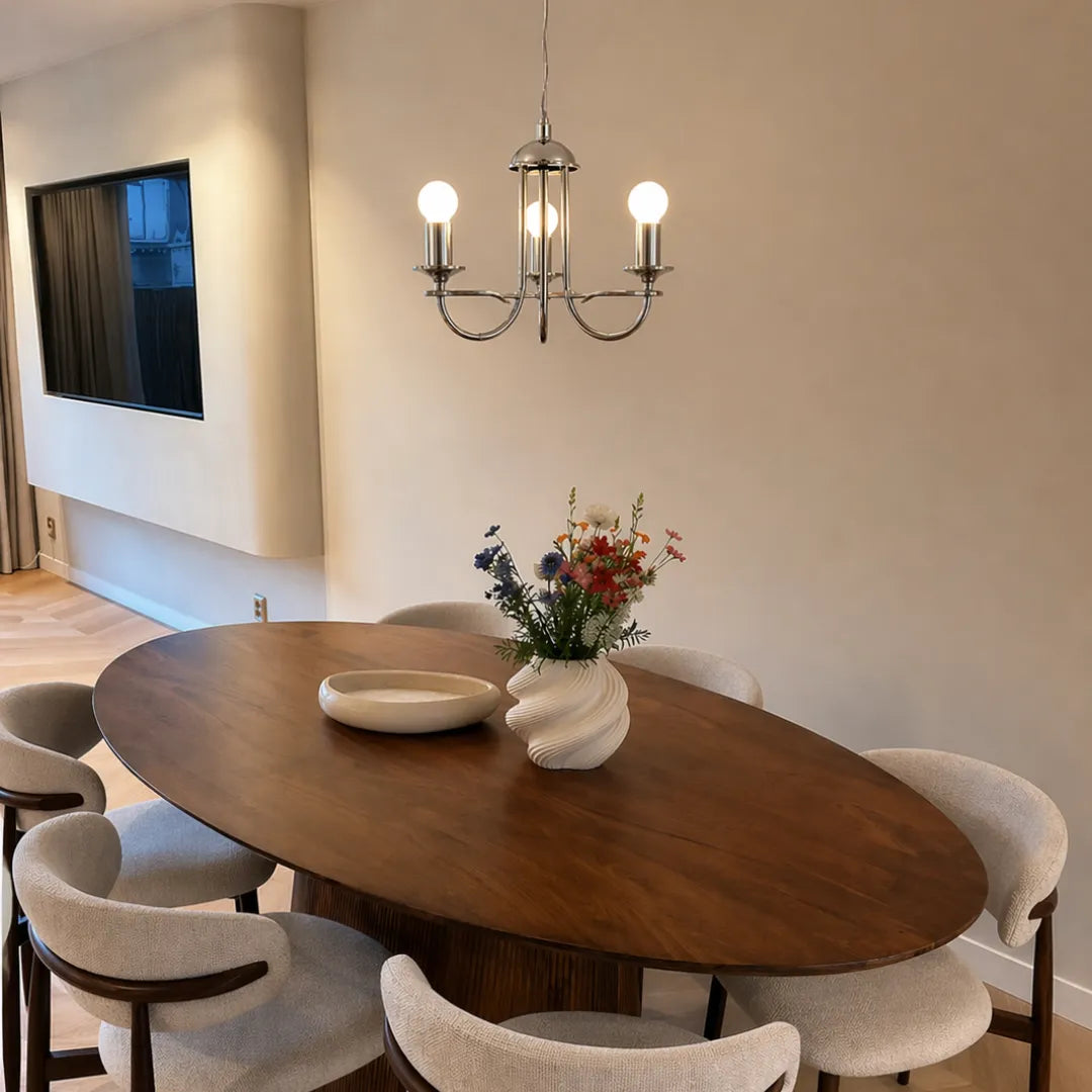 Lustre pendente cromado aceso sobre mesa oval de madeira em sala de jantar com cadeiras estofadas e vaso de flores — Lustre Pendente Vela Rústico Industrial 3 Luzes Brant — Tonzi